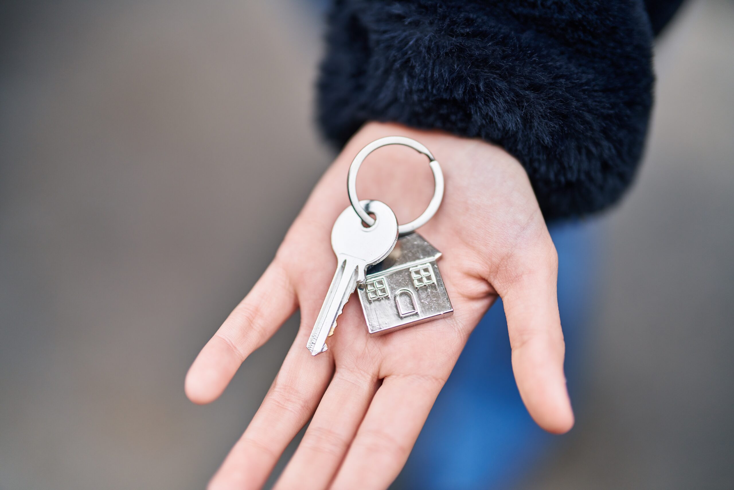 Young woman holding key of new home at street Young woman holding key of new home at street